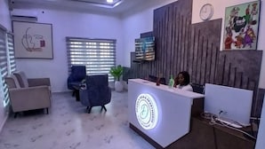 A reception desk with a logo, a clock, and a TV on the wall. There are two chairs and a potted plant in the room. - Devon's 5BR Villa with Pool, Gym & Bar, gated in Katampe Abuja (Abuja)