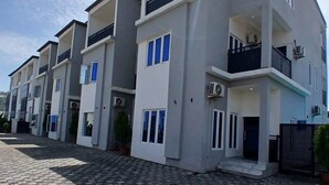A modern multi-story residential building with balconies, air conditioning units, and a paved driveway. - Devon's 5BR Villa with Pool, Gym & Bar, gated in Katampe Abuja (Abuja)