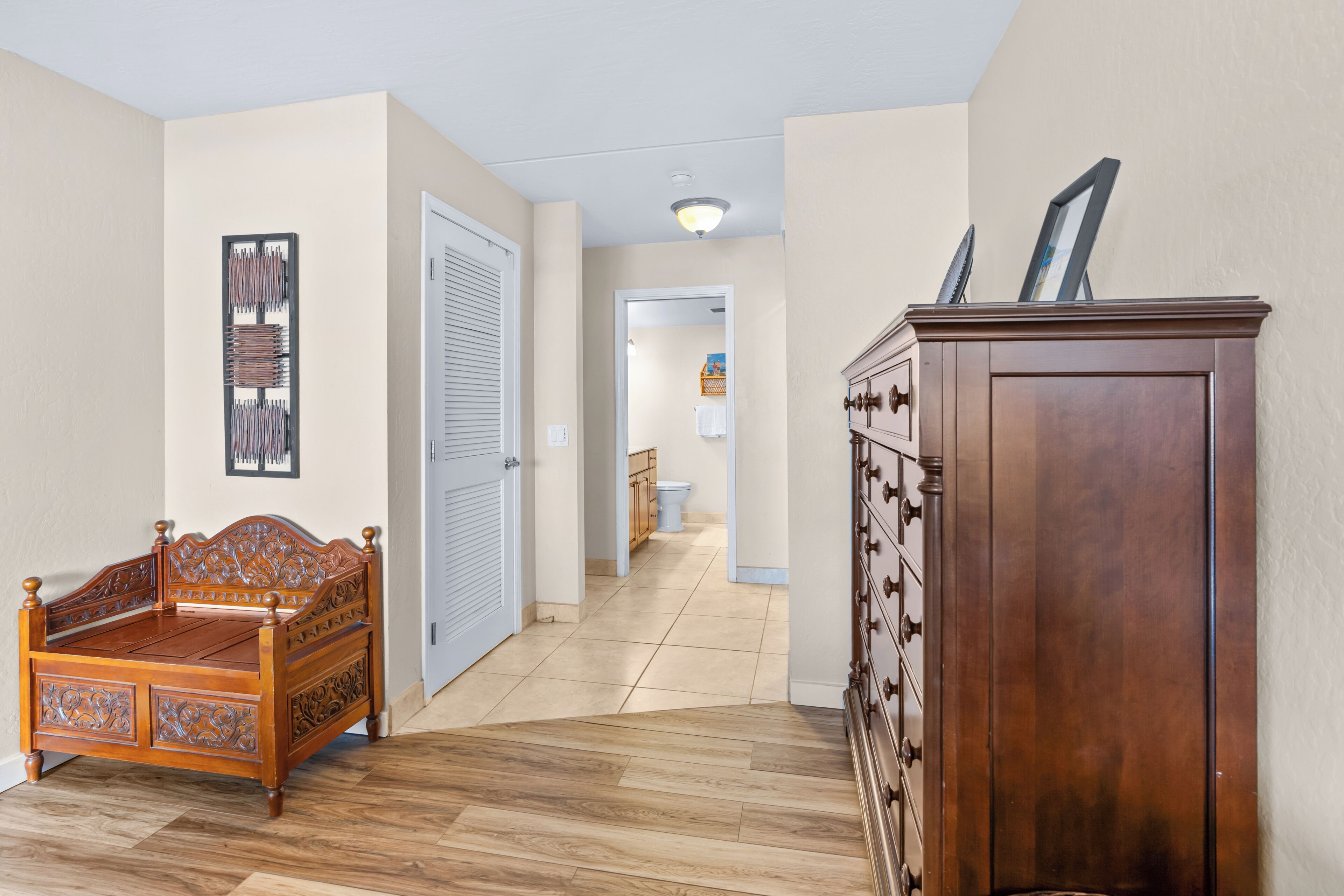 A hallway with a wooden bed, a dresser, and a door leading to a bathroom.