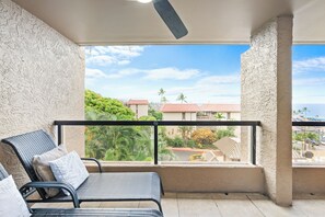Ein Balkon mit Blick auf eine Wohngegend, einem Deckenventilator und einem Sessel mit Kissen.