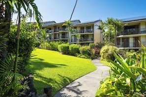 A hotel with multiple balconies, lush greenery, and a well-maintained lawn. - Kona Makai 3-102, Ocean View, Air Conditioning (Kailua Kona)