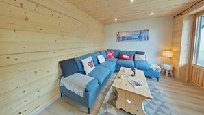 Interior acogedor de una cabaña con techo de madera, un sofá modular azul, una mesita y un cuadro en la pared.