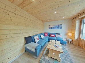 Ein gemütliches Blockhaus-Interieur mit Holzbalkendecke, einem blauen Modulsofa, einem kleinen Tisch und einem Gemälde an der Wand.