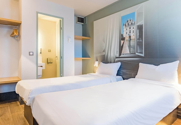 A hotel room with two beds, a painting of a building, a wooden shelf, and a door leading to another room.