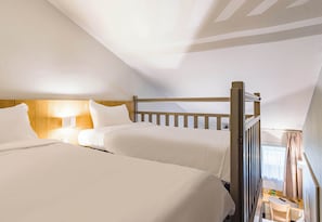 Quarto de hotel com duas camas, cabeceiras de madeira, uma mesinha e uma janela com cortinas.
