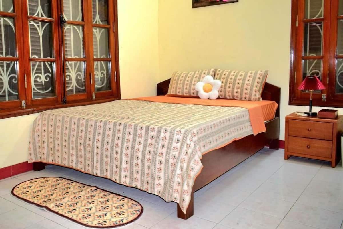 Un dormitorio con cama, una mesita de noche, lámpara, almohada decorativa, alfombra y un cuadro en la pared.