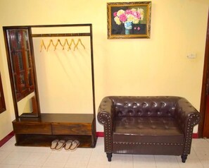 Ein Zimmer mit einem dunkelbraunen Ledersofa, einem Holz-Waschtisch mit Spiegel und einem gerahmten Blumenbild an der Wand.