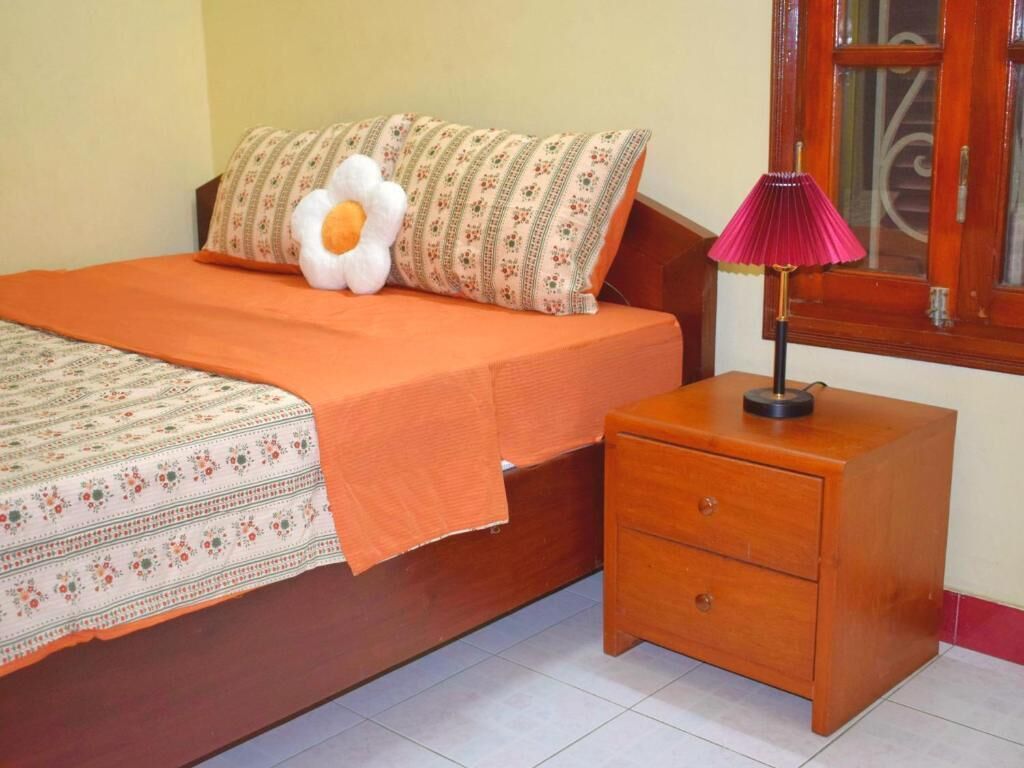 A bedroom with a bed, a nightstand, a lamp, a window, and a patterned bedspread.
