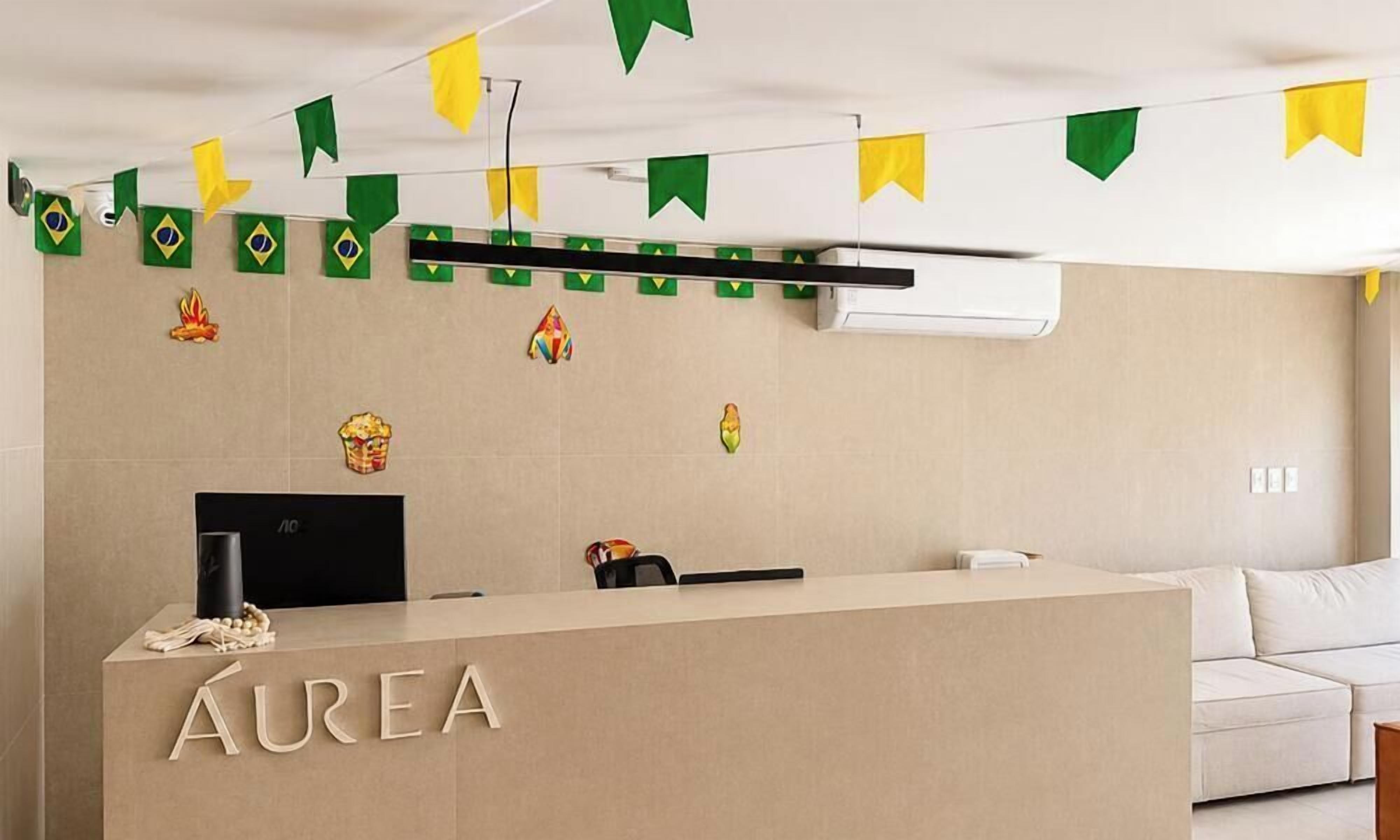 A reception desk with the name 'AUREA' in the center, a white sofa to the right, and a wall with decorative tiles and a mounted air conditioner.