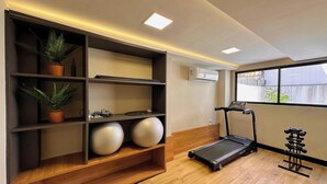 A gym with exercise equipment, a treadmill, and shelves with exercise balls and plants. - Bauten Aurea - LikeHome  (João Pessoa)
