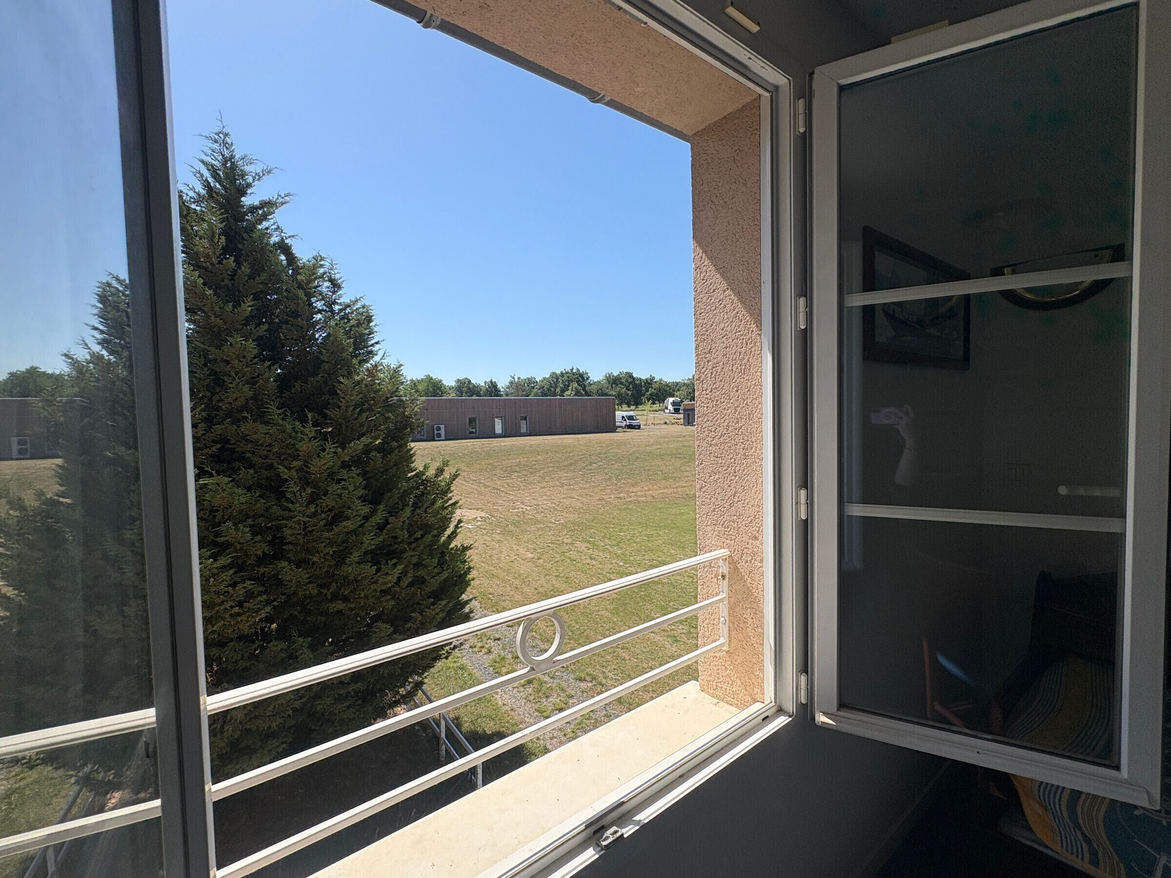A balcony with a clear view of a grassy field and a building in the distance.