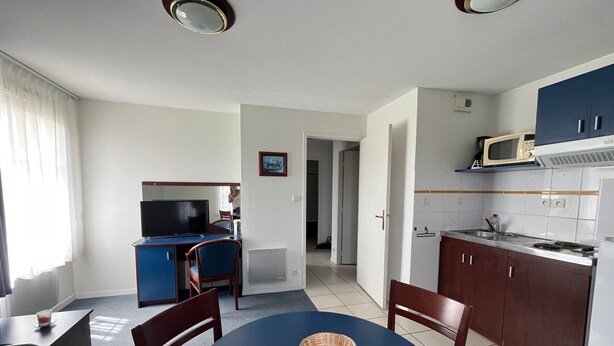 Un ambiente compatto con angolo pranzo, televisione, cucina con microonde e una porta che conduce a un'altra stanza.