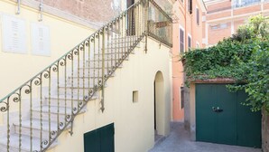 A narrow alleyway with a metal staircase leading to a building entrance, a green door, and a wall with electrical boxes. - Apartment via Monte del Gallo (Roma)