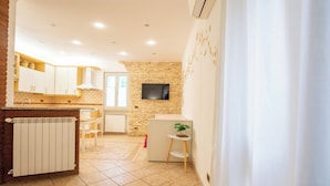 A kitchen with white cabinets, a stone wall, a TV, and a small table with a plant. - Apartment via Monte del Gallo (Roma)