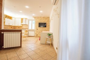 Eine Küche mit weißen Schränken, einer Steinwand, einem Fernseher und einem kleinen Tisch mit einer Pflanze.