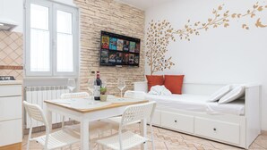 A modern room with a dining table, white chairs, a sofa with red cushions, a TV mounted on a stone wall, and a decorative tree decal. - Apartment via Monte del Gallo (Roma)
