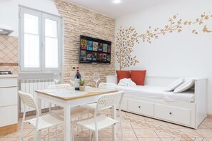 Ein modernes Zimmer mit einem Esstisch, weißen Stühlen, einer Couch mit roten Kissen, einem an einer Steinwand montierten Fernseher und einer dekorativen Baum-Abziehbild.