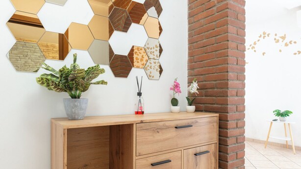 A wooden desk with drawers, a potted plant, and a wall-mounted hexagonal mirror. - Apartment via Monte del Gallo (Roma)