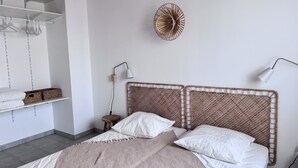 A bedroom with a bed, a bedside table, a lamp, a wall-mounted shelf, and a hanging rack. - The Oceanid (Saint-Denis-d'Oléron)