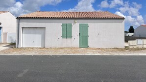A single-story building with a tiled roof, a closed white garage door, and a green door. - The Oceanid (Saint-Denis-d'Oléron)