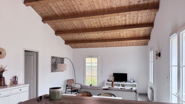 A modern kitchen with wooden beams, a dining area with a sofa, and a TV. - The Oceanid (Saint-Denis-d'Oléron)