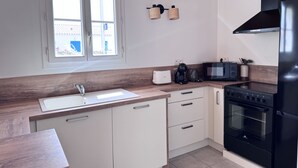A kitchen with a window, white cabinets, a black stove, and a microwave. - The Oceanid (Saint-Denis-d'Oléron)