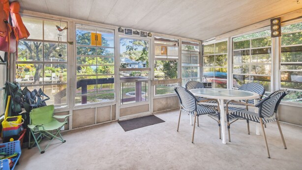 Un patio techado con mesa y sillas, amplias ventanas y vistas al exterior.