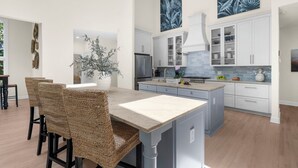 Una cucina moderna con mobili bianchi, un'isola centrale e un'area pranzo con sedie in vimini.