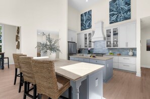 Eine moderne Küche mit weißen Schränken, einer zentralen Kochinsel und einem Essbereich mit Korbstühlen.