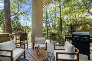 Una terraza con mobiliario exterior, una parrilla y vista a árboles.