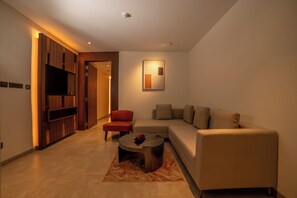 A modern living room with a sofa, a red chair, a coffee table, and a TV mounted on a wooden panel. - RG Grand Hotel & Convention (Bengaluru)