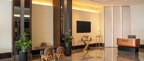 Um saguão de hotel moderno com balcão de recepção, área de estar e uma grande televisão de tela plana.