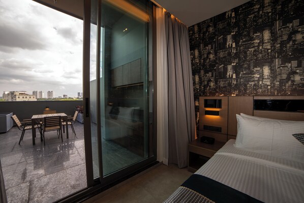 A hotel room with a large sliding glass door leading to an outdoor seating area, a cityscape view, a bed with white linens, and a city-themed wallpaper. - RG Grand Hotel & Convention (Bengaluru)