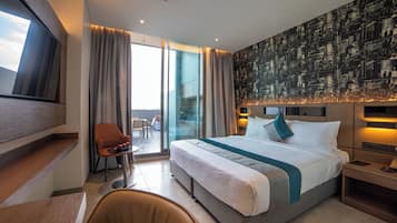 Ein modernes Hotelzimmer mit einem großen Bett, einem Fernseher, einem Schreibtisch und einem Balkon mit Blick auf die Stadt.