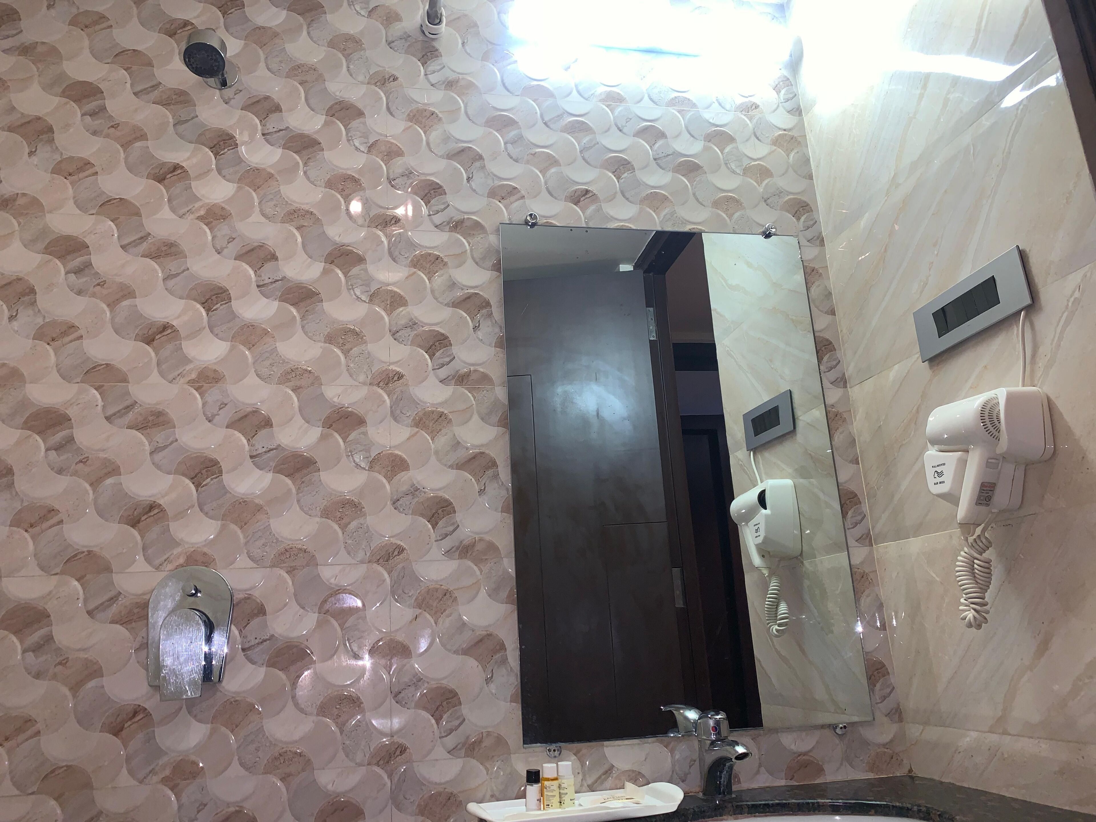 Ein Badezimmer mit Musterwand, einem Spiegel, einem Waschbecken, einem Föhn und einem Handtuchhalter.