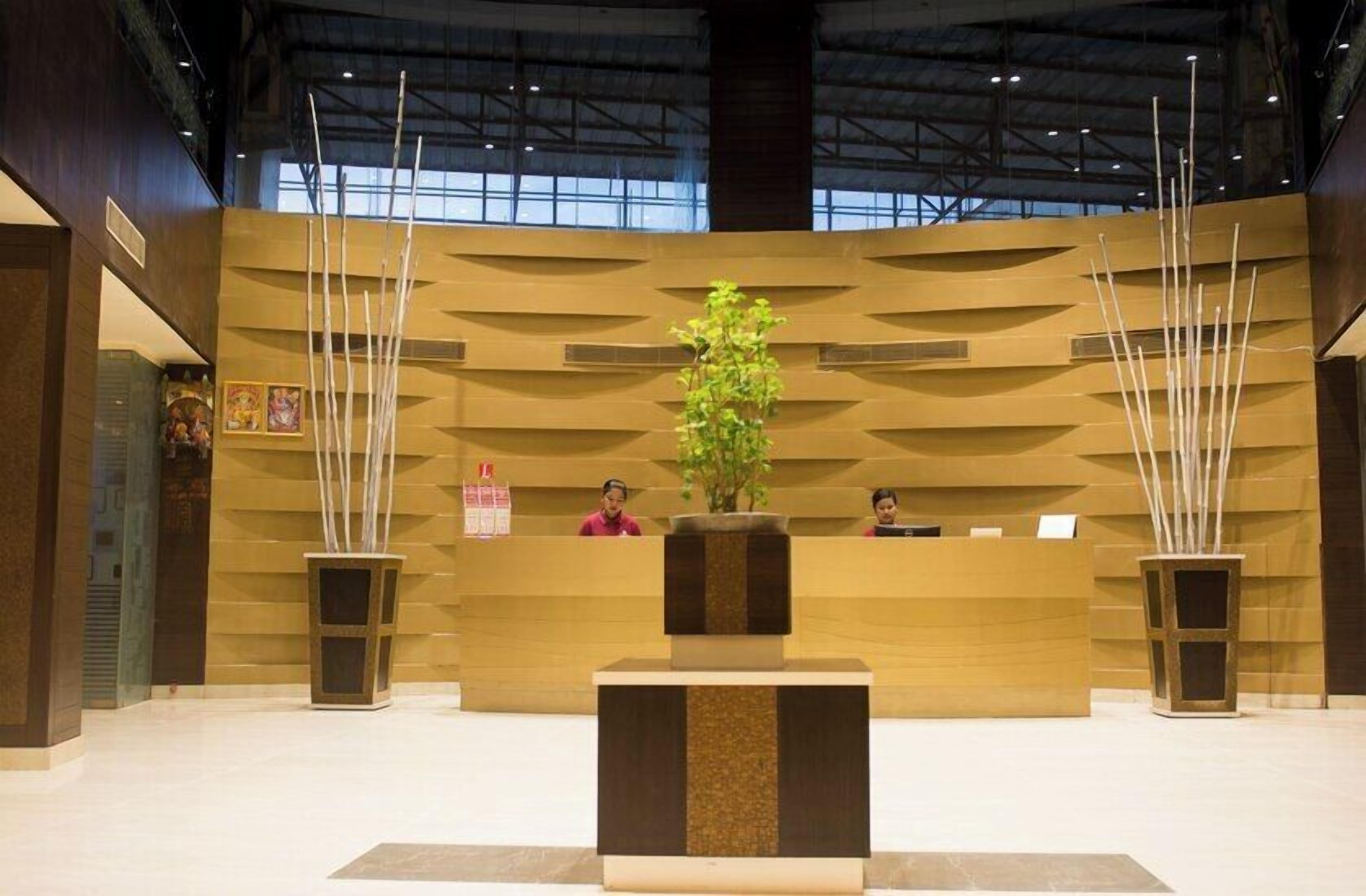 A reception area with a reception desk, two plants, and a high ceiling.