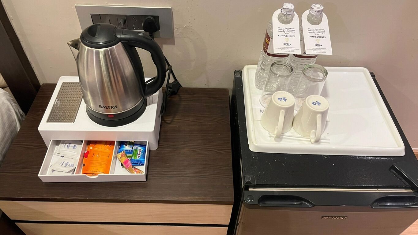 A hotel room with a coffee maker, tea set, and a drawer with toiletries.