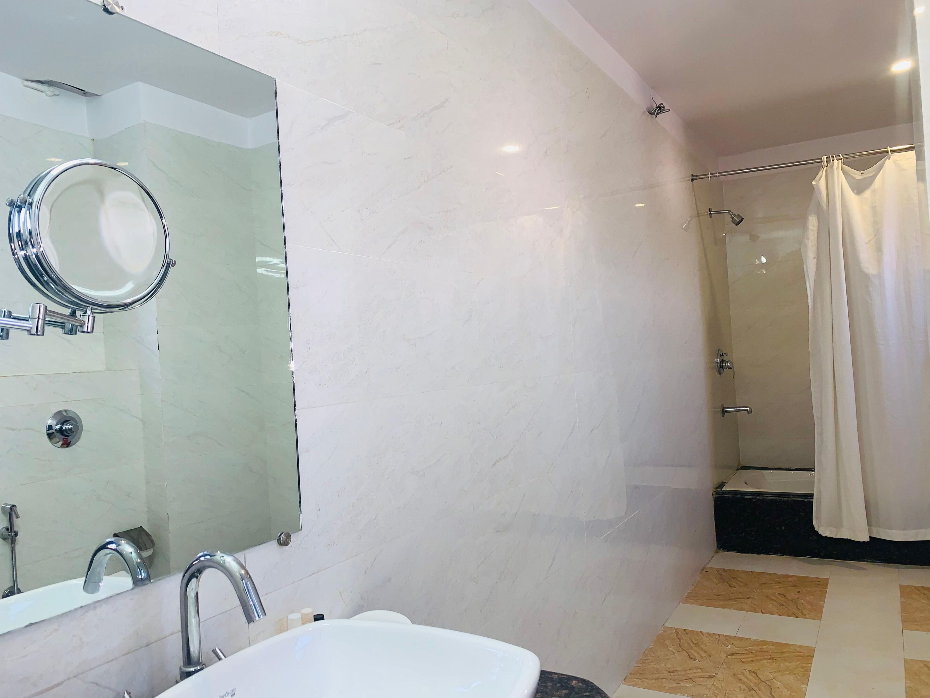 A bathroom with a sink, mirror, shower, and a tiled floor.