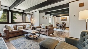 Ein geräumiges Wohnzimmer mit einer großen Couch, einem Couchtisch und einem Sessel. Im Hintergrund ist ein Essbereich mit Tisch und Stühlen zu sehen.
