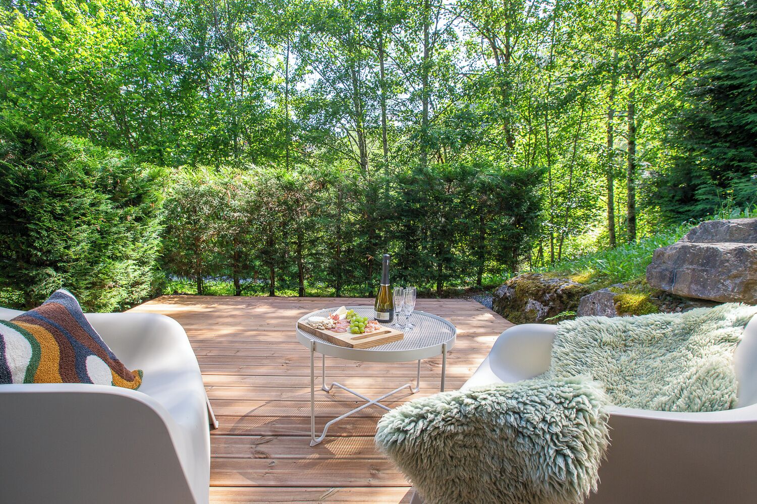 Een terras buiten met een ronde tafel, witte stoelen en een plaid.