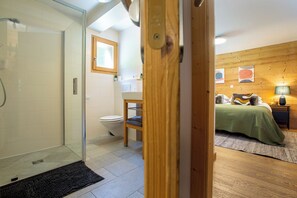 Ein Badezimmer mit Duschkabine aus Glas, Toilette und Holzfenster.