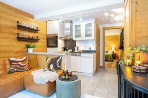 Ein gemütliches Wohnzimmer mit einer Couch, einem Couchtisch und einer Küchenzeile mit Schränken und Geräten.