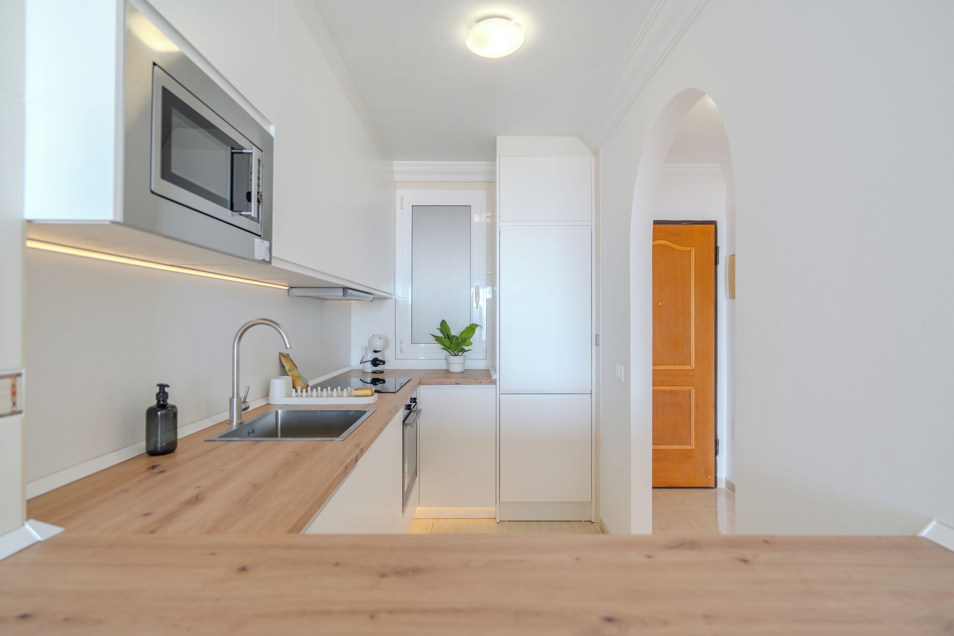 A modern kitchen with a wooden countertop, stainless steel sink, and a microwave.