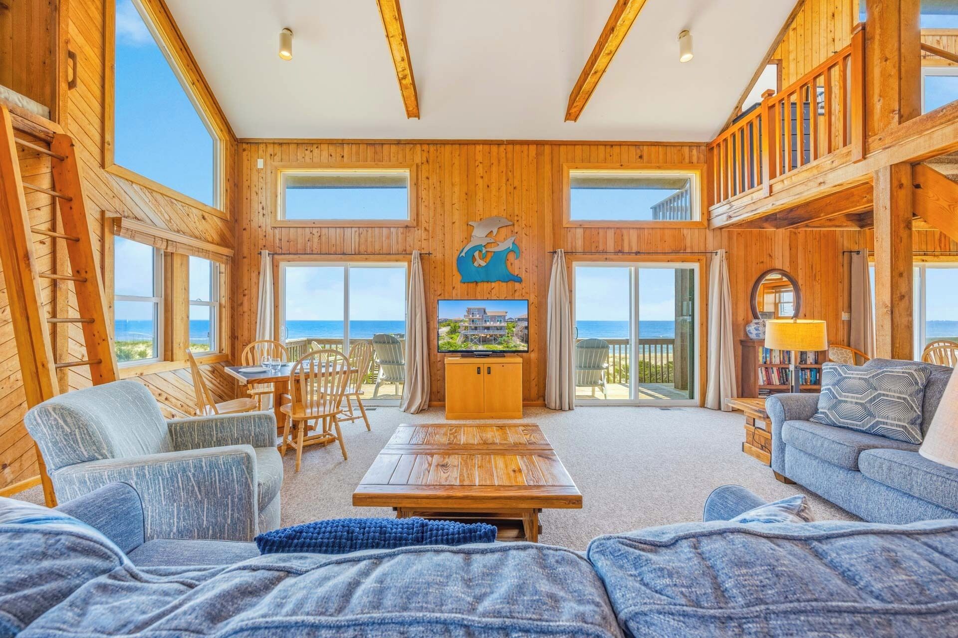 A wooden interior with a dining area, a television, and a balcony with a view of the sea.