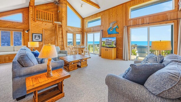 A spacious living area with wooden walls, a large TV, and a view of the ocean. - Oceanfront, Dog Friendly Home in Avon with Boardwalk to the Beach (Avon)