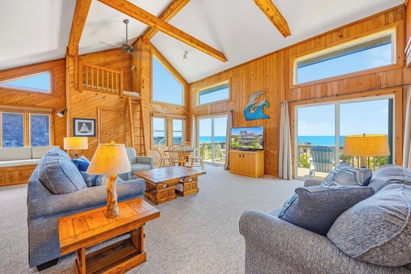 Ein geräumiges Wohnzimmer mit Holzwänden, einem großen Fernseher und Blick auf den Ozean.