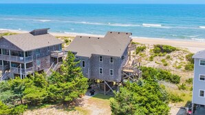 A beachfront property with multiple buildings, including a two-story house with a balcony and a smaller structure on stilts, overlooking the ocean. - Oceanfront, Dog Friendly Home in Avon with Boardwalk to the Beach (Avon)