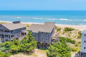 Ein Strandgrundstück mit mehreren Gebäuden, darunter ein zweistöckiges Haus mit Balkon und eine kleinere Konstruktion auf Stelzen, mit Blick auf den Ozean.
