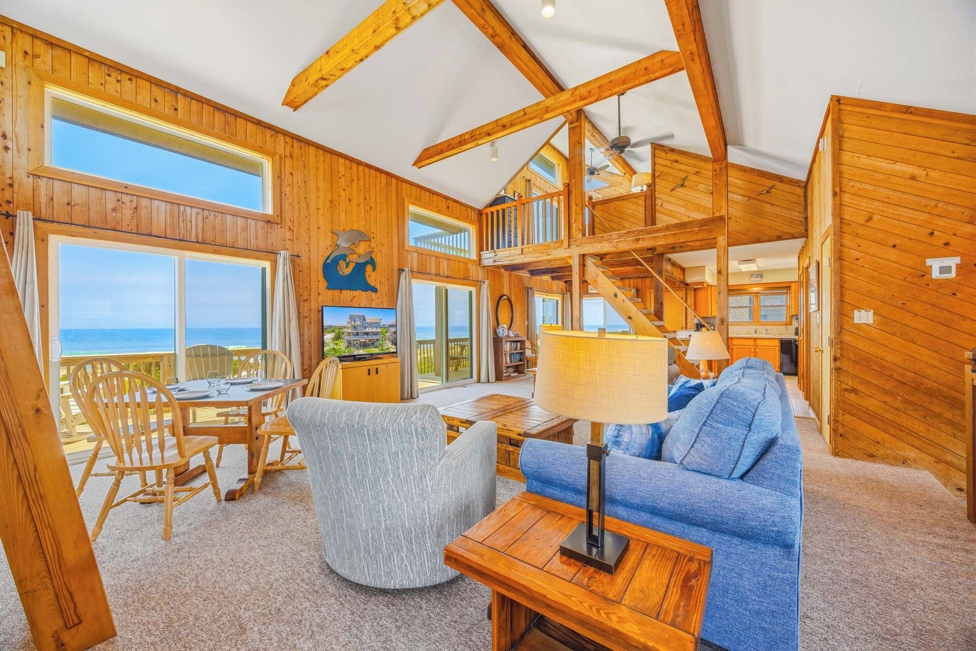 A wooden interior with a dining area, a sofa, a TV, and a staircase leading to an upper level.
