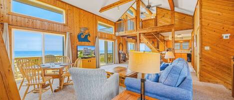 A wooden interior with a dining area, a sofa, a TV, and a staircase leading to an upper level.